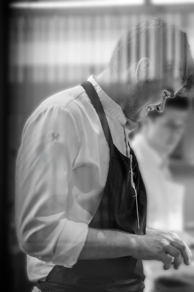 Chef Nathan Campbell geconcentreerd aan het werk in de keuken — zwart-wit portret